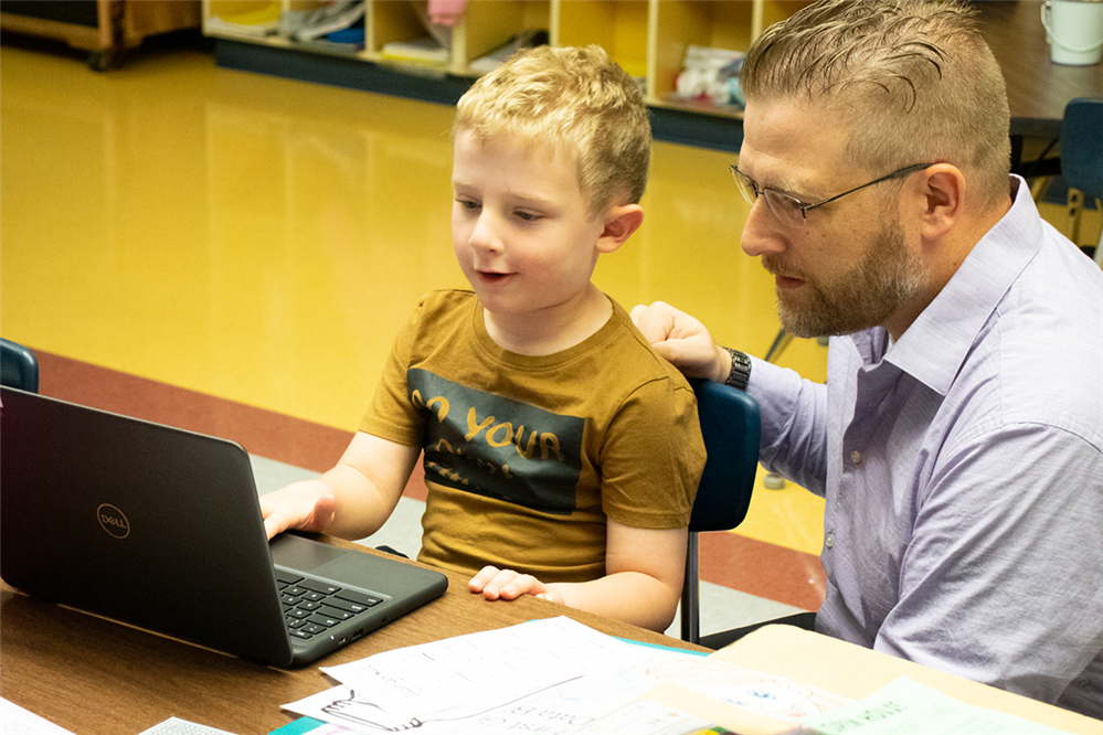 A student smiles at a laptop computer